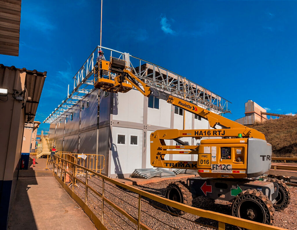 Plataforma elevatória articulada Haulotte HA16 RTJ sendo usada para montagem de estrutura metálica em um módulo multipavimentos.